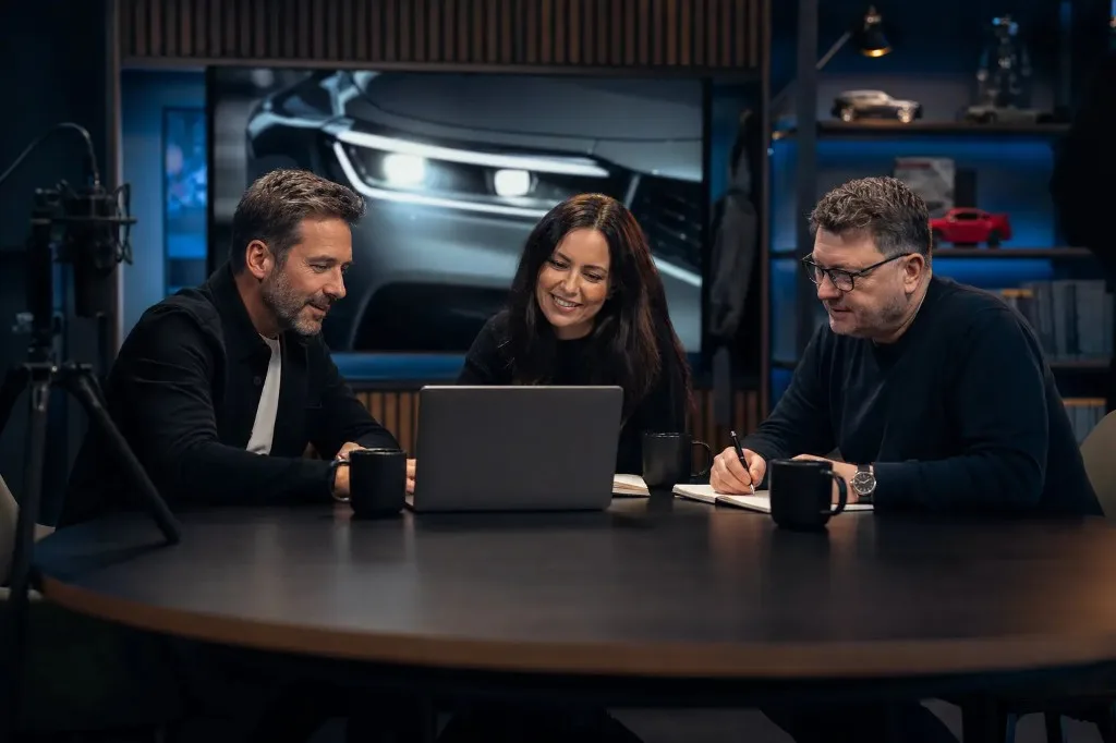 Equipo editorial colaborando en reunión con un coche de fondo
